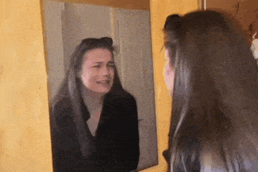 a woman is looking at herself in a mirror .