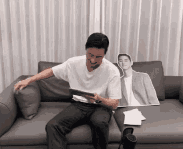 a man is sitting on a couch with a cardboard cutout of him