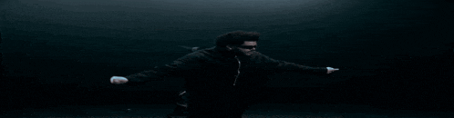 a man wearing sunglasses and a black jacket is dancing in a dark room .