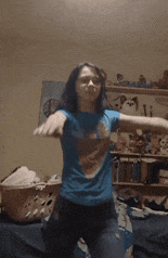 a girl in a blue shirt is dancing in front of a laundry basket on a bed