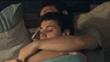 two men are hugging each other in bed with their eyes closed .