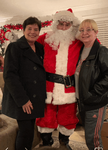 two women are posing for a picture with a man dressed as santa claus