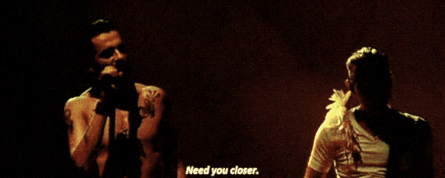 a man singing into a microphone next to another man with the words need you closer