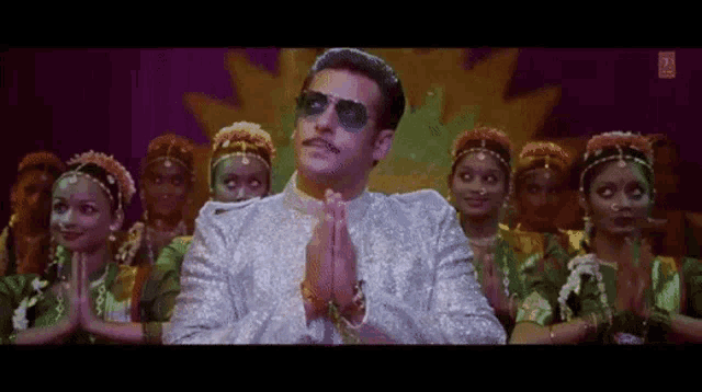 a man wearing sunglasses is praying in front of a group of women .