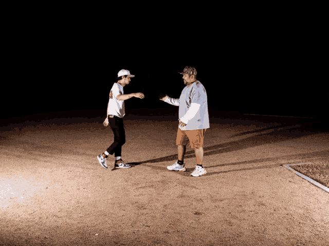 a man and a boy are standing on a dirt field in the dark