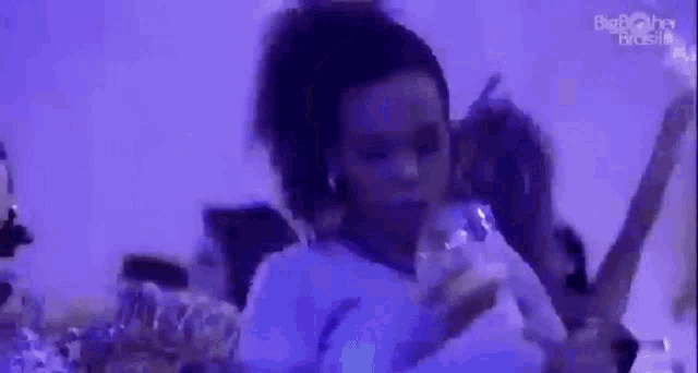 a woman is sitting on a bed in a dark room holding a glass of water .