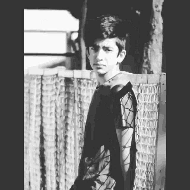 a black and white photo of a boy standing next to a fence