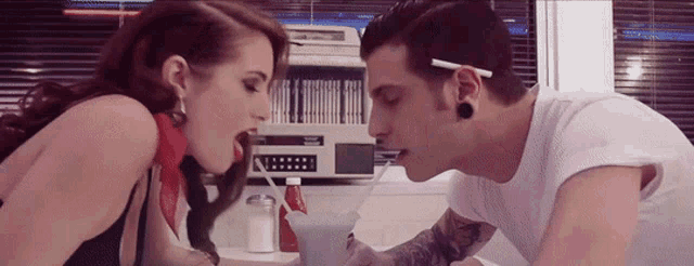 a man and a woman are drinking milkshakes from the same cup