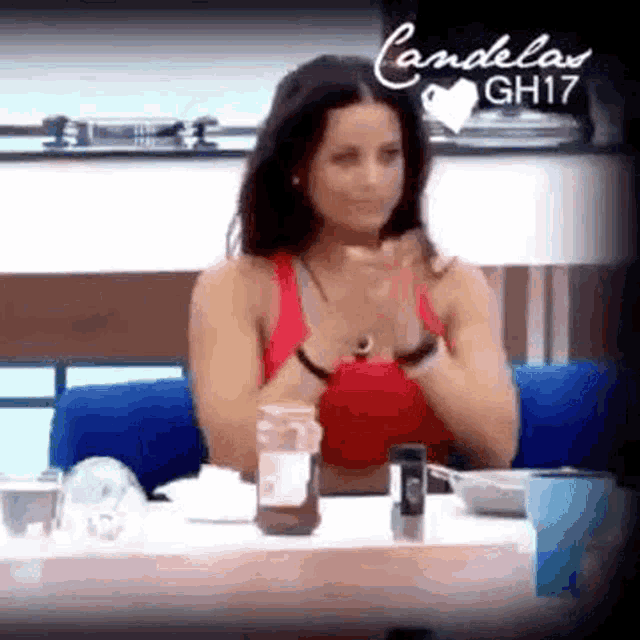 a woman in a red tank top is sitting at a table with her hands folded .