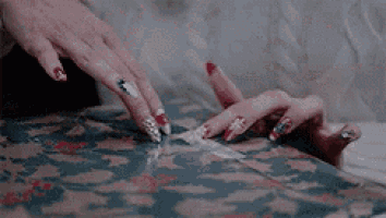a close up of a woman 's hands with long nails reaching for something on a couch .