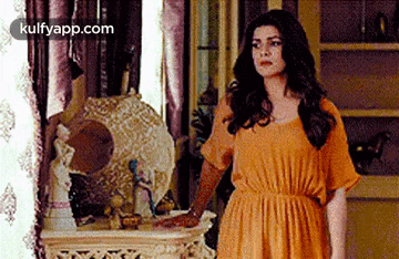 a woman in an orange dress is standing in a room next to a mirror .