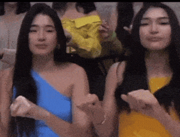 two women are standing next to each other and one is wearing a blue top and the other is wearing a yellow dress