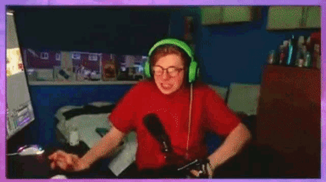 a young man wearing green headphones and glasses is sitting in front of a computer .