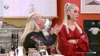 two women are standing in a kitchen with their arms crossed and one is wearing a red dress