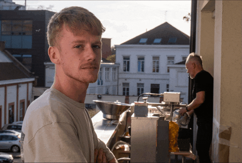 a man stands in front of a machine while another man stands behind him