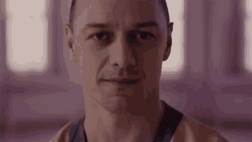 a close up of a man 's face with a purple background looking at the camera .