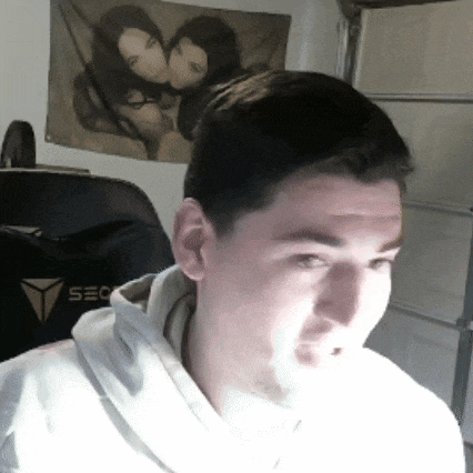 a man wearing a white hoodie is sitting in front of a wall with a picture of two women on it .