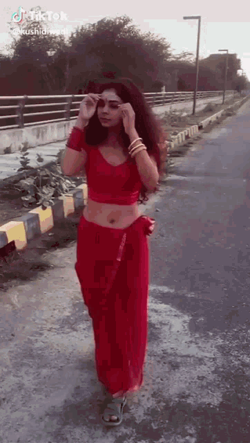 a woman in a red crop top and skirt is walking down a street .