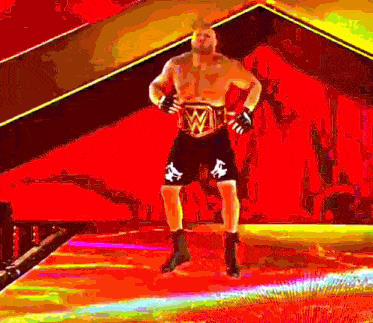 a wrestler is standing on a stage with his hands on his hips wearing a wrestling belt