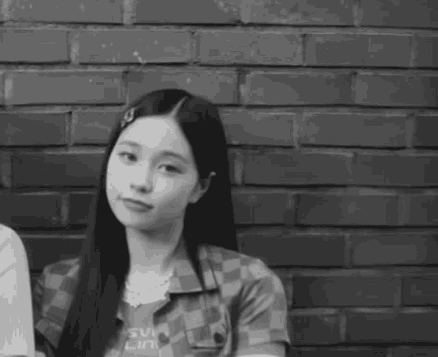 a black and white photo of a woman standing in front of a brick wall wearing a shirt that says sw lin