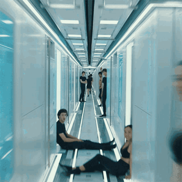 a group of people are sitting on the floor in a long hallway