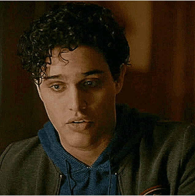 a young man with curly hair is making a funny face while wearing a gray jacket and a blue shirt .
