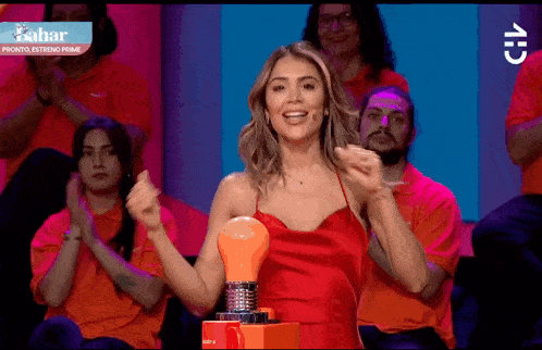 a woman in a red dress is holding a light bulb in front of a group of people