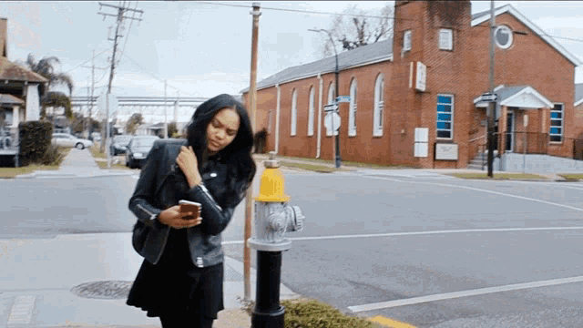 a woman is standing next to a fire hydrant and looking at her phone