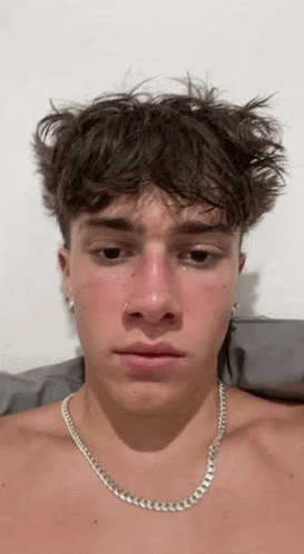 a shirtless young man wearing a silver chain around his neck is making a sad face .
