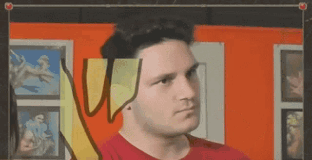 a man in a red shirt stands in front of an orange wall with a drawing of a banana on it