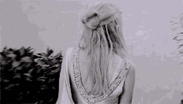 a woman with long hair is standing in a field of tall grass blowing in the wind .