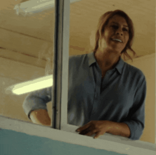 a woman in a blue shirt is smiling while looking out a window