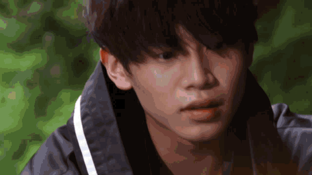 a close up of a young man 's face with a gray jacket on