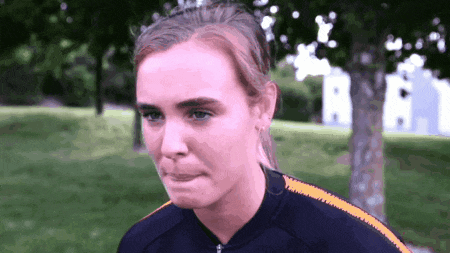 a woman wearing a black jacket with orange stripes on the sleeves is making a sad face