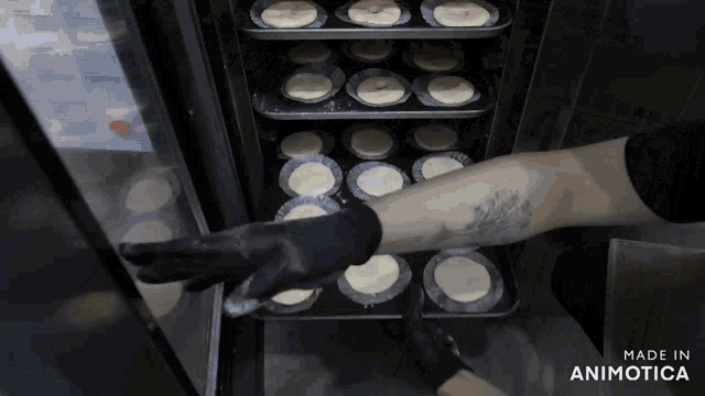 a person wearing black gloves reaches into a tray of cupcakes made in animotica