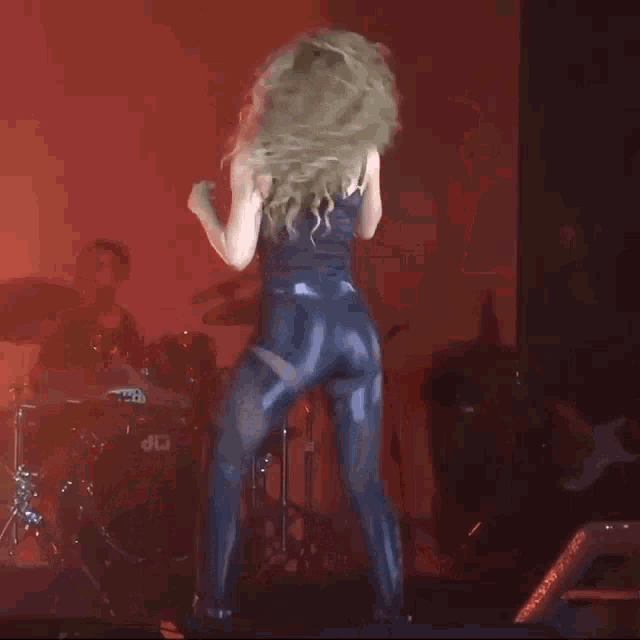 a woman with curly hair is dancing on a stage in front of a drum set .