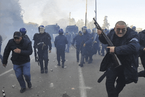 a man holding a shotgun in front of a crowd of riot police