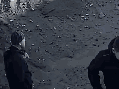 two men are standing next to each other on a dirt road . one is wearing a blue hat .