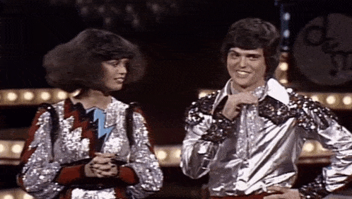 a man and a woman are standing next to each other on a stage and the man is wearing a sequined shirt