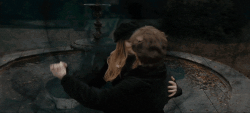 a man and woman are hugging in front of a water fountain