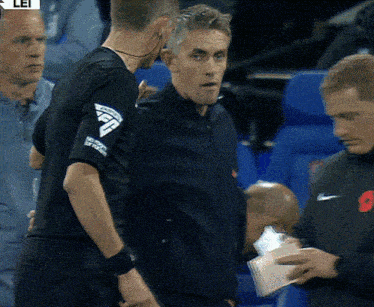 a man wearing a black shirt with the letter f on the sleeve talks to another man