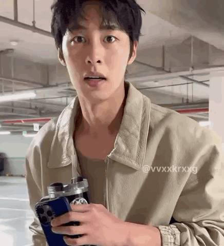 a man in a tan jacket is holding a cell phone and a water bottle .