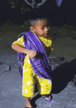 a young boy wearing a yellow shirt and purple shorts holds a purple scarf around his neck
