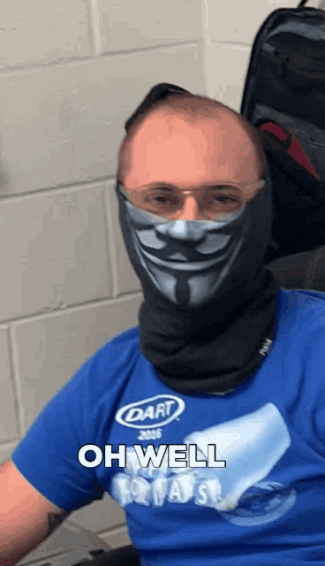 a man wearing a dart shirt and a face mask says oh well