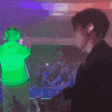 a man in a green hoodie stands in front of a crowd at a concert
