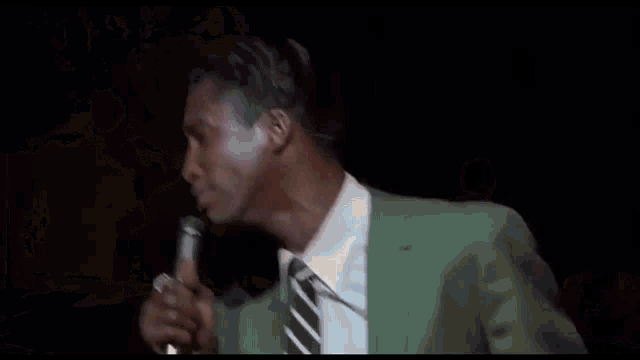 two men in suits and ties are singing into microphones on a stage .