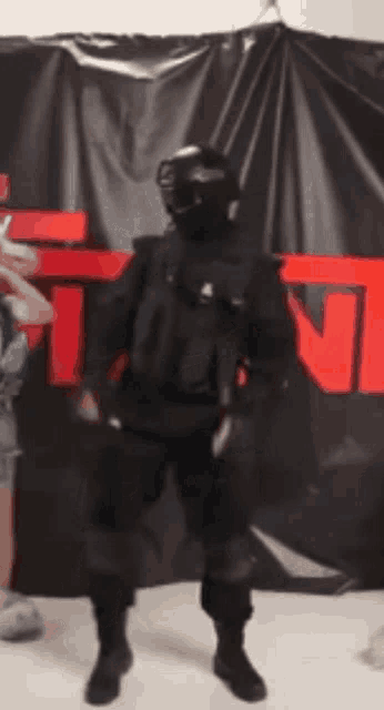 a man in a military uniform is standing in front of a black curtain with the letter t on it .