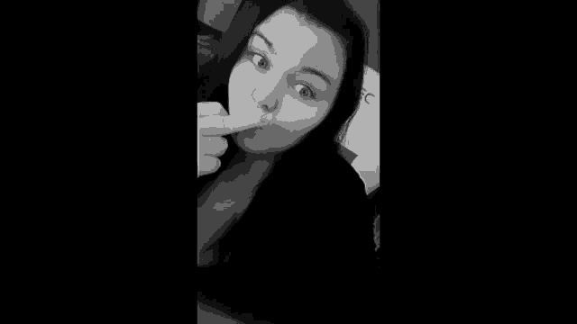 a black and white photo of a young woman taking a selfie with her finger in her mouth .