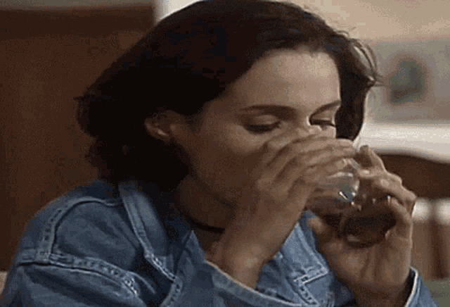 a woman wearing a denim jacket is drinking from a glass