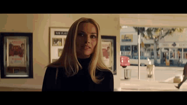 a woman in a black turtleneck is standing in front of a window with a sign that says no parking